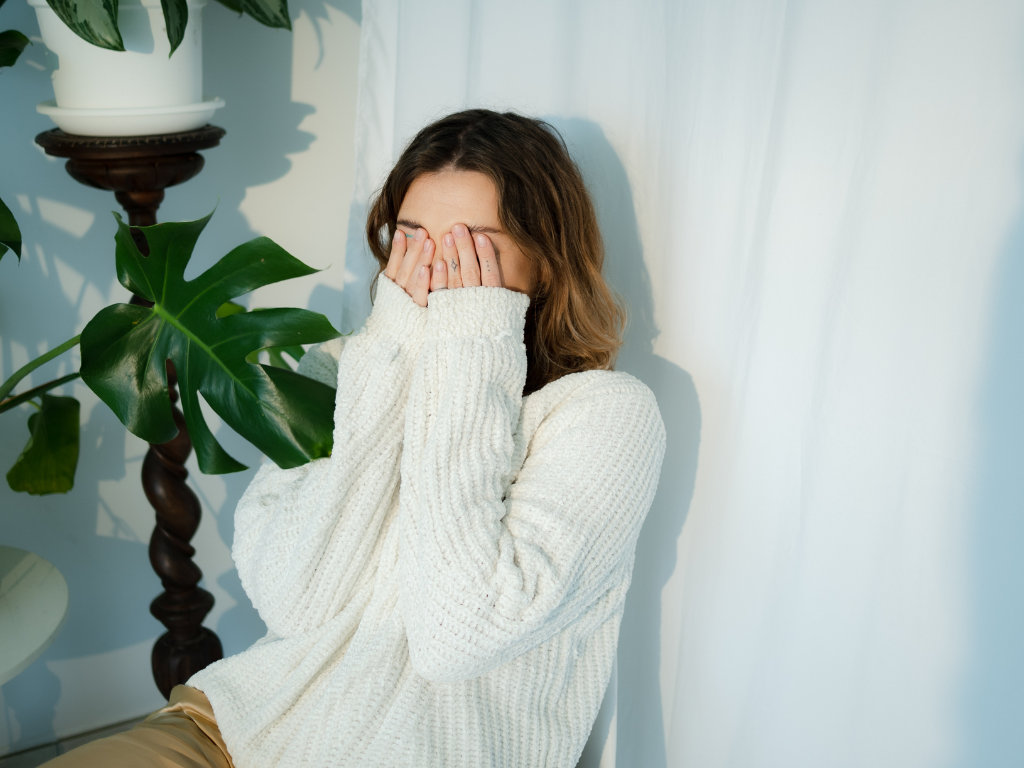 Shy woman in a cream jumper covering her face with her hands