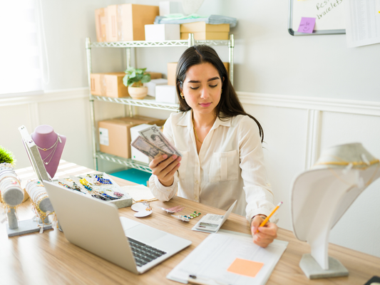 Small business owner counting cash at her desk with a laptop