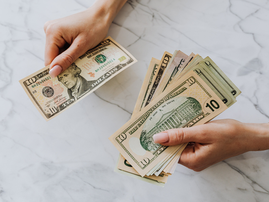 Hands counting ten dollar bills on a marble table